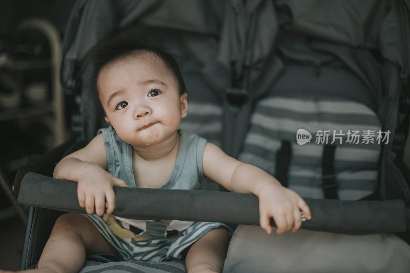 asian chinese baby boy sitting in the stroller waiting for parent going for a walk in the park morning